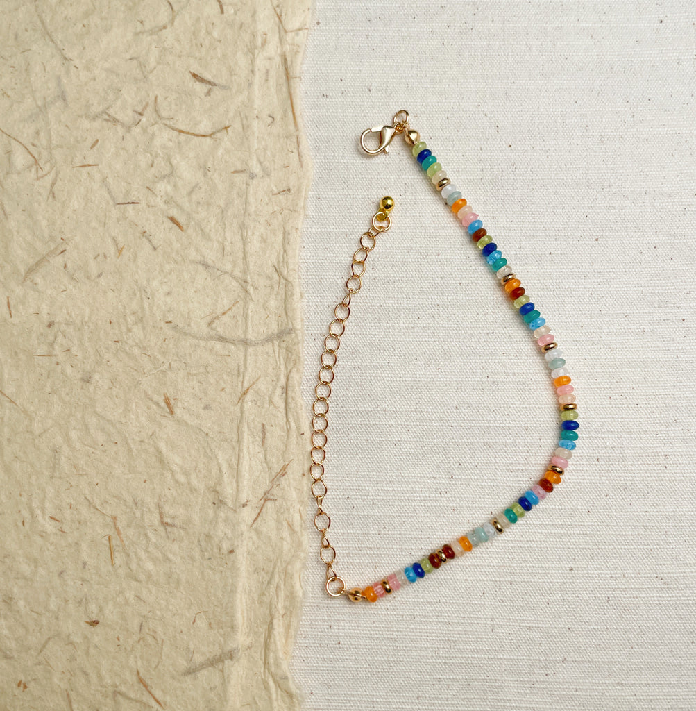 Colorful glass bead bracelet on wrist, dainty gold chain boho jewelry.