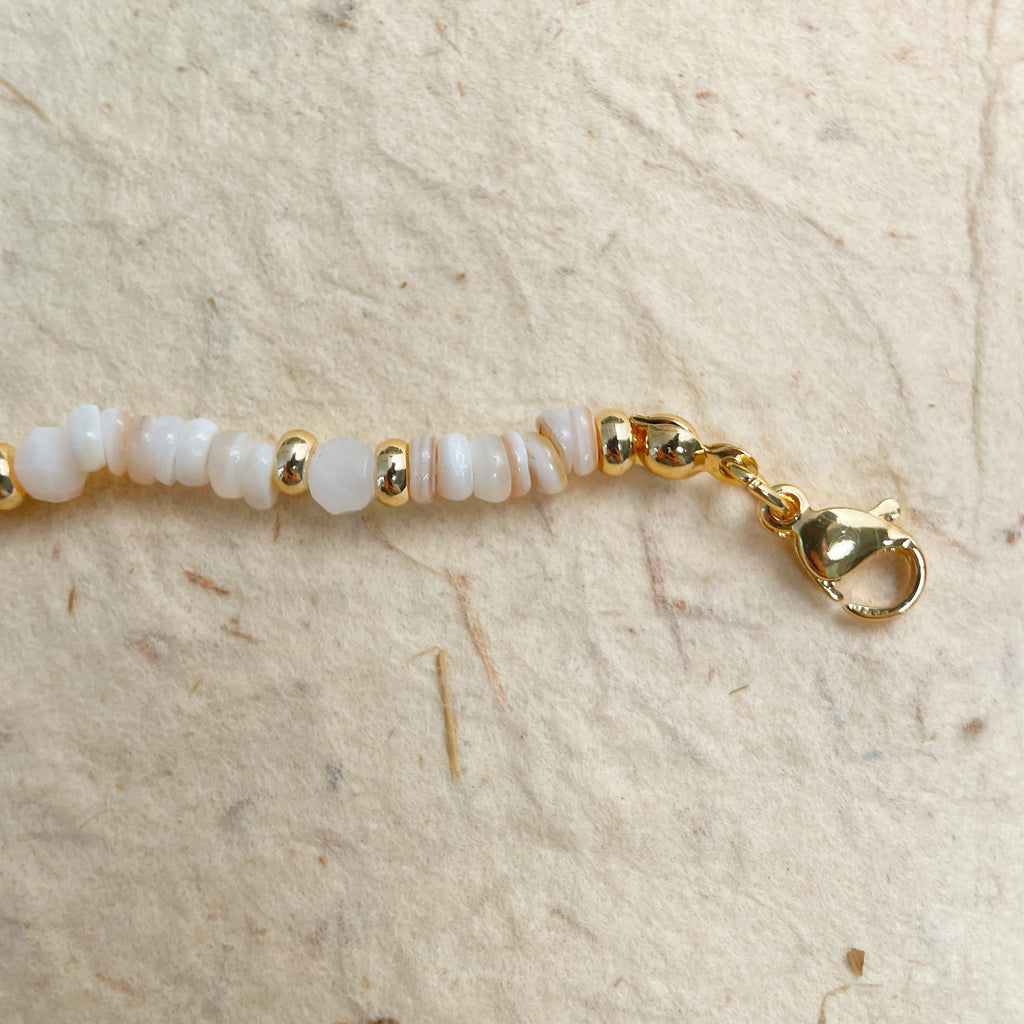 Bracelet with white beads and gold clasp on a beige background