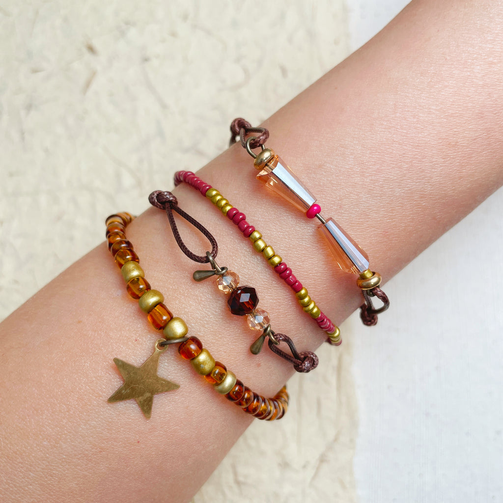 Layered glass bead bracelets on wrist, warm tone boho star charm jewelry.