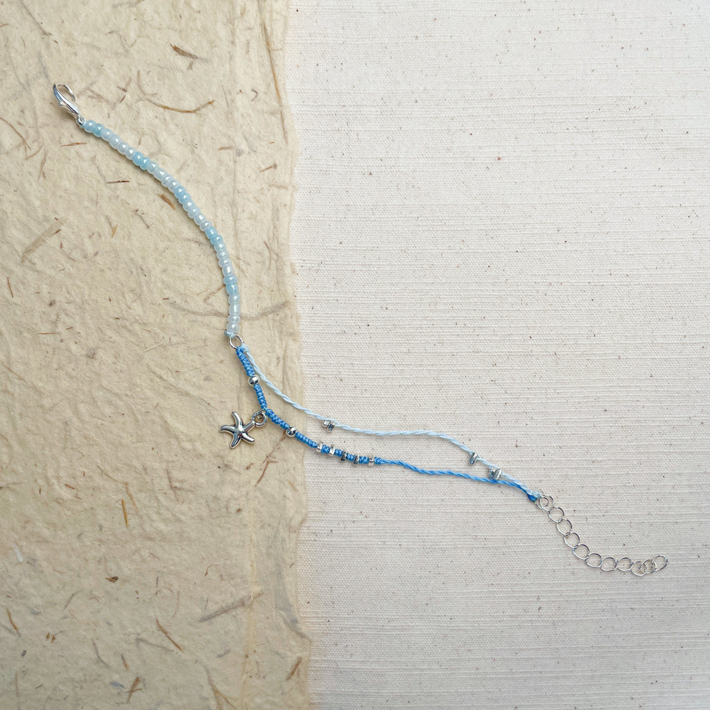 Adjustable blue glass bead bracelet on wrist, starfish charm summer jewelry.