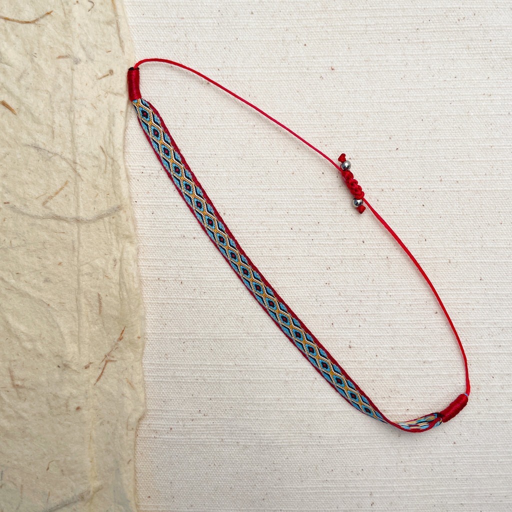 Woven red string bracelet with geometric pattern, adjustable boho friendship jewelry.