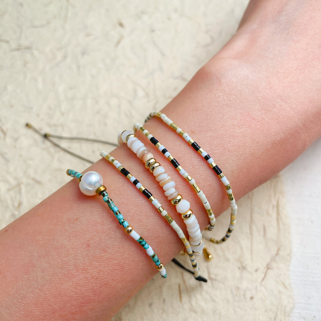 Adjustable seed bead wrap bracelet on wrist, layered black and gold boho jewelry.