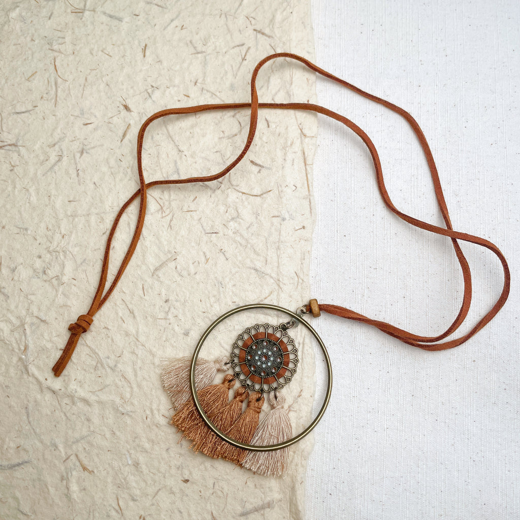 Handmade boho necklace with circular metal pendant and brown tassels on leather string