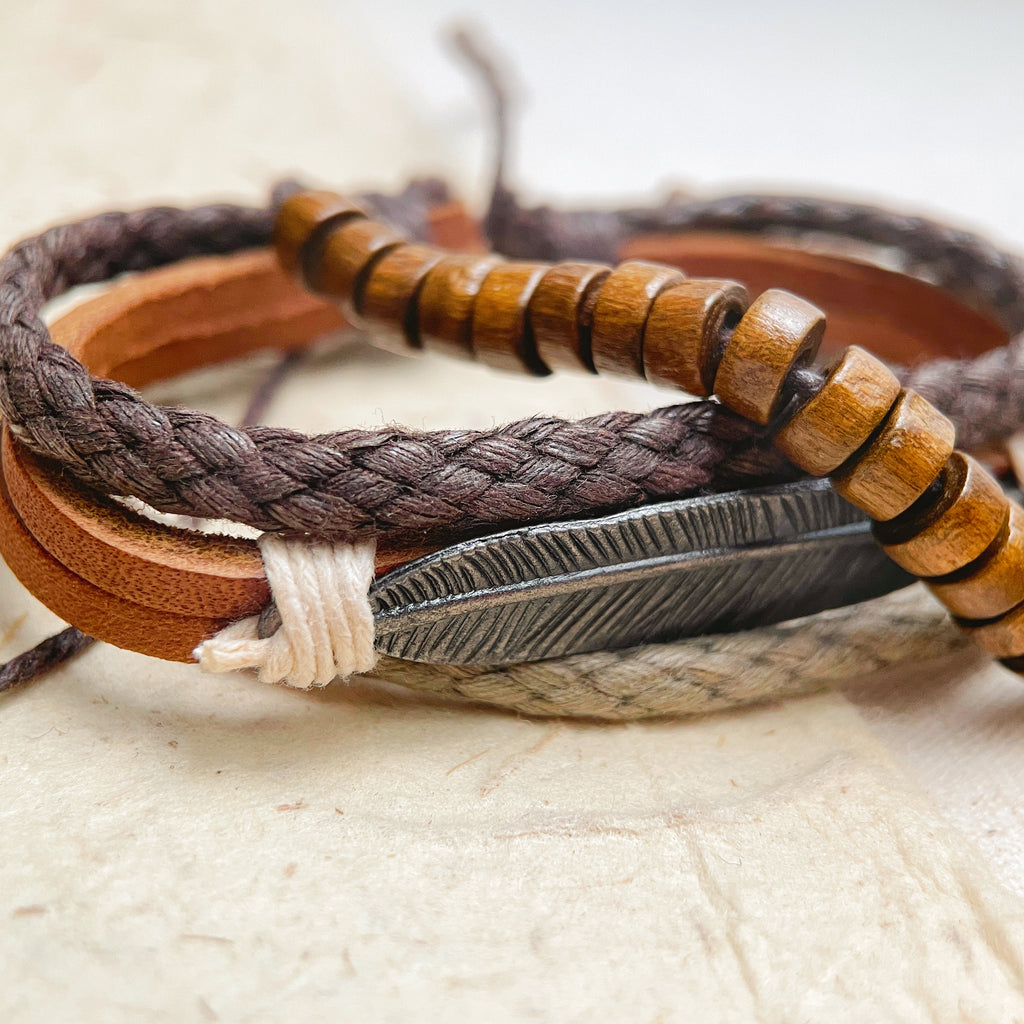 Layered leather and wood bracelet on wrist, rustic feather charm jewelry for men.