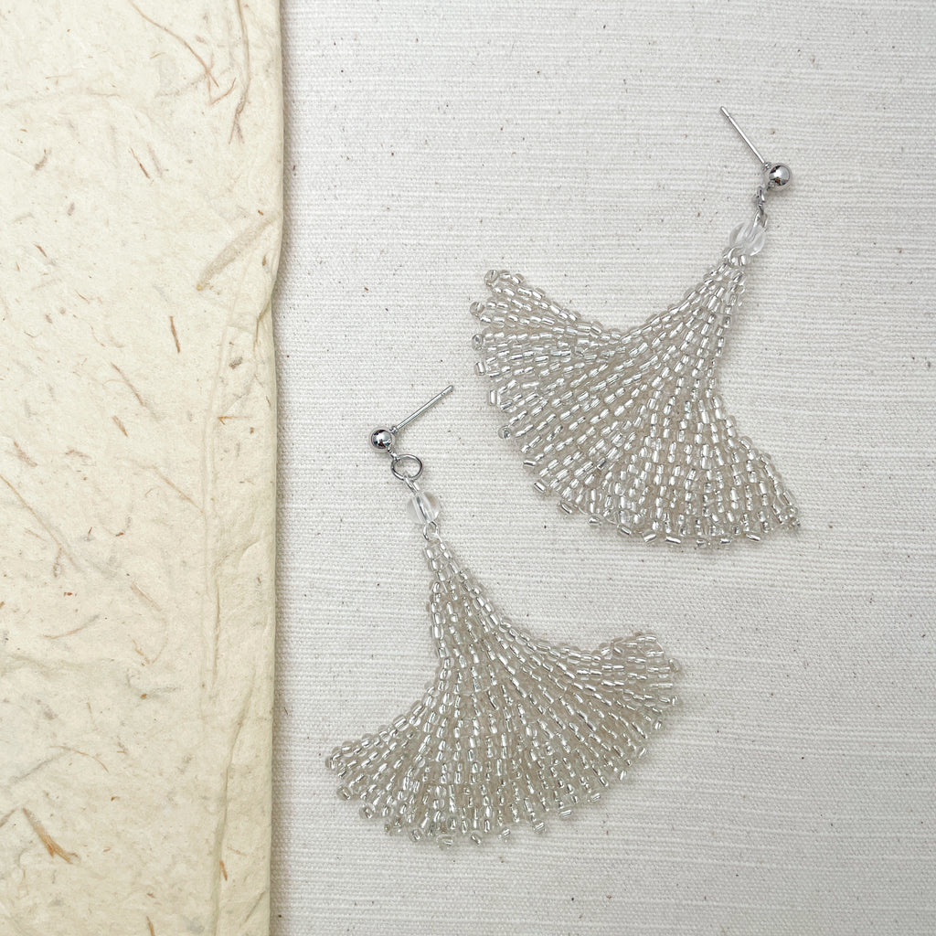 Handcrafted silver earrings featuring cascading clear glass beads, shown in a soft, textured setting.
